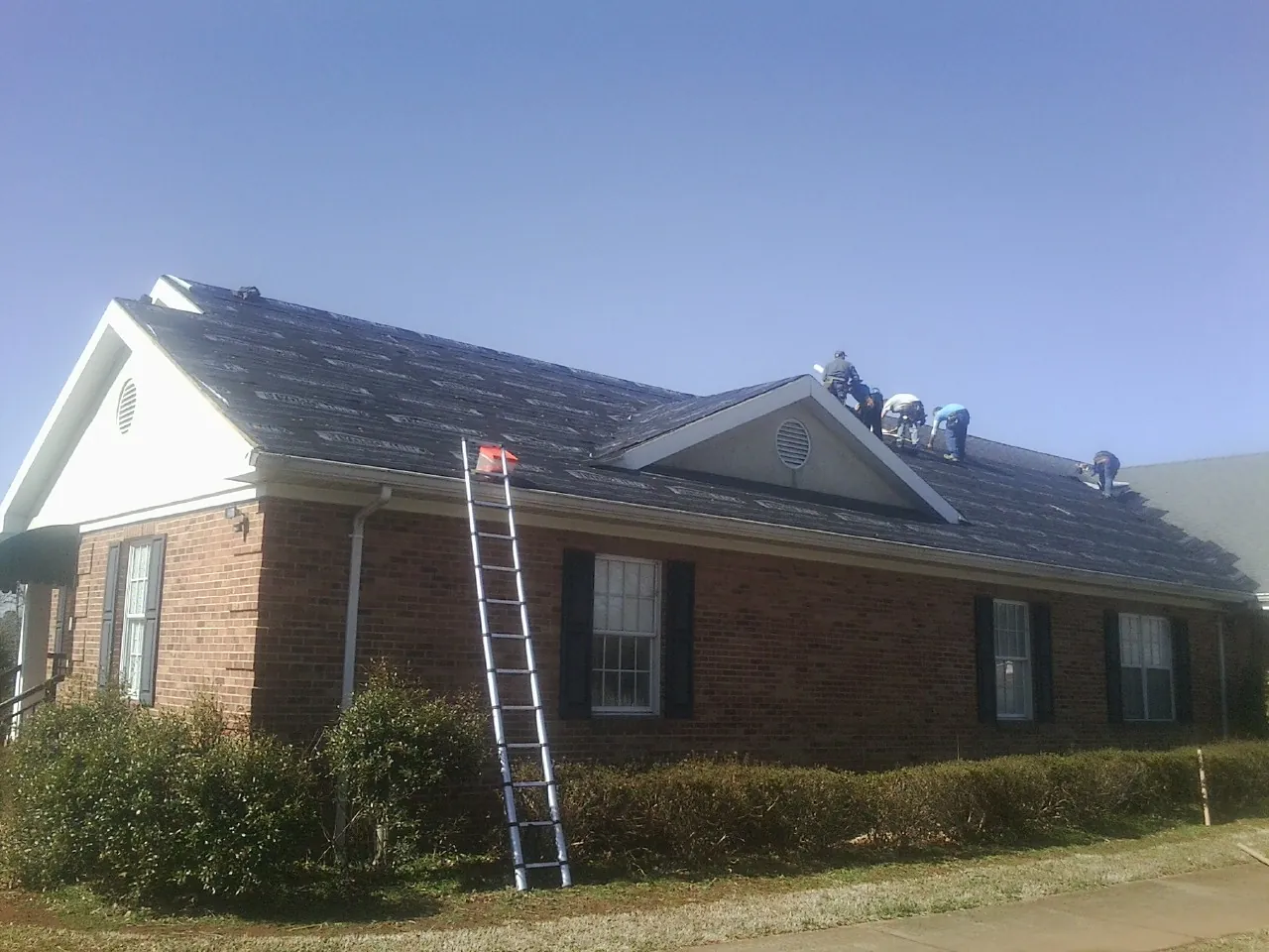 Crew tearing shingles off a brick ranch roof with a ladder set — Metal Roof Repair work by our crew in Artesia