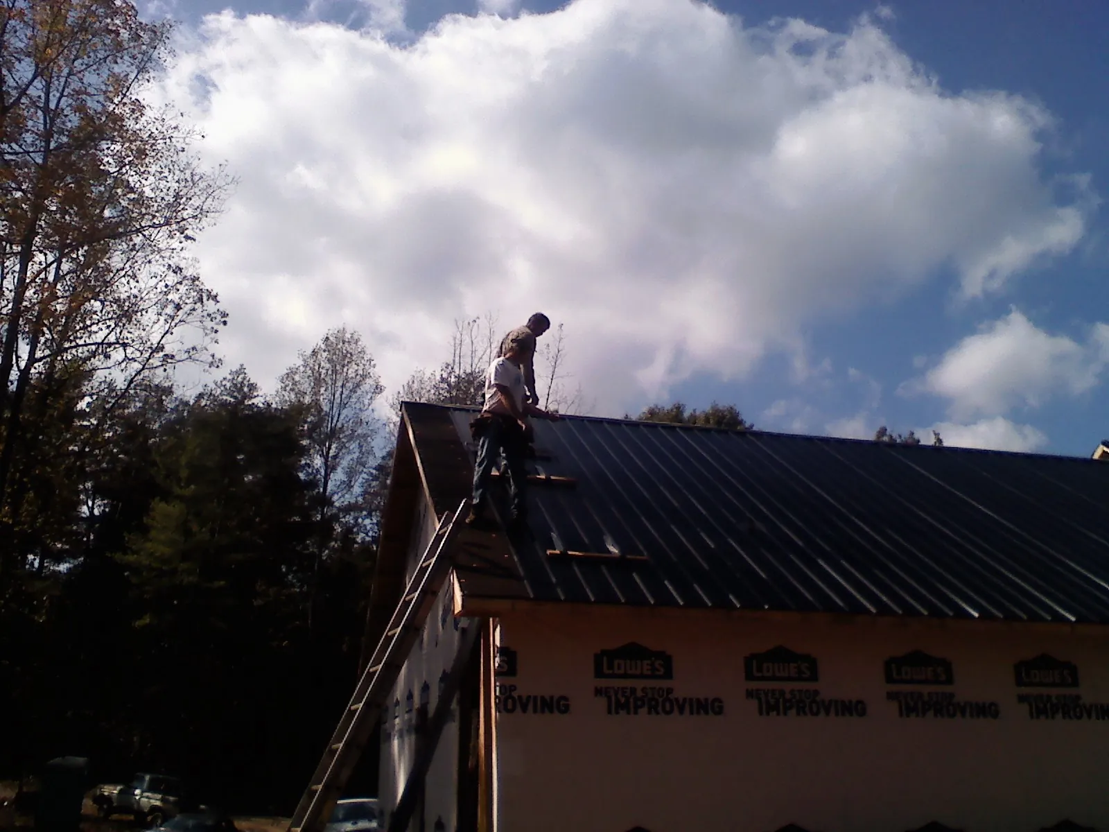Roofer fastening dark metal panels high against a cloudy sky, from a Roof Inspection job in Artesia