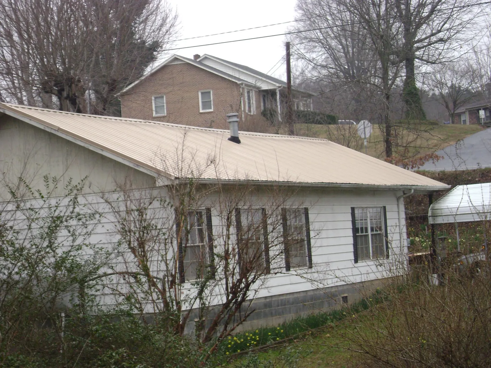 Tan metal roof on a white sided house set into a hillside — Commercial Roofing by Roofing Brothers in Artesia