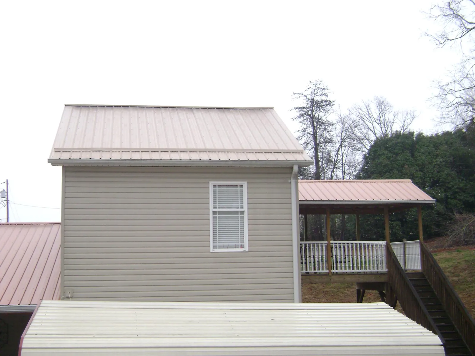 Tan metal roofs on a two story addition and attached porch in Artesia